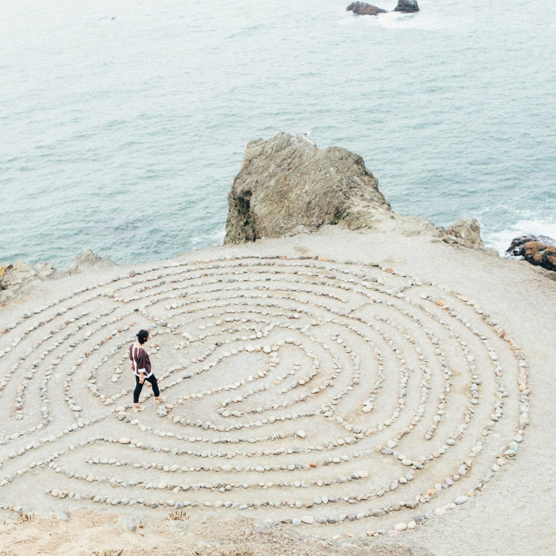 Overhead view of Woman walking into a serene made of small stones on a sandy beach maze overlooking the calm ocean